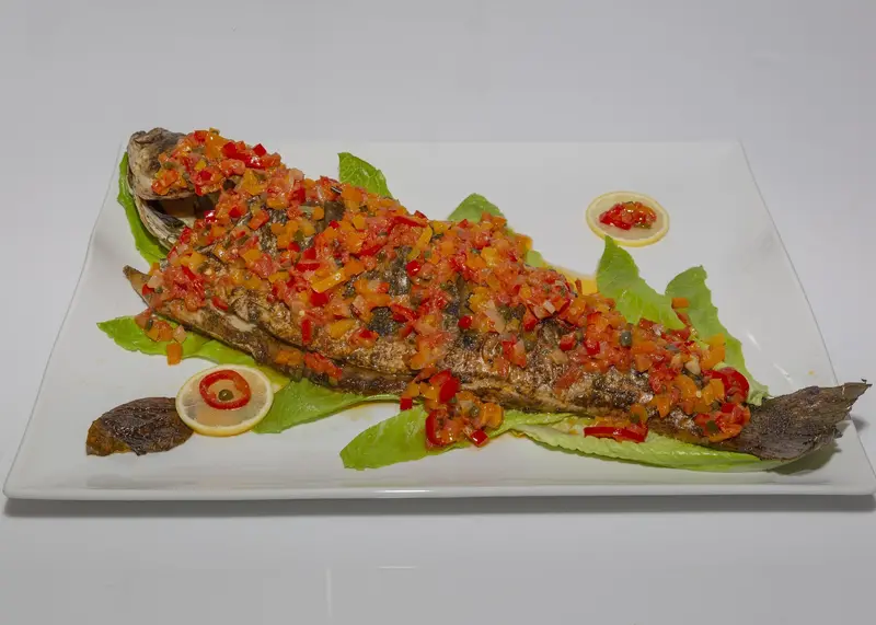 Whole rockfish covered in a colorful pepper relish on a long platter